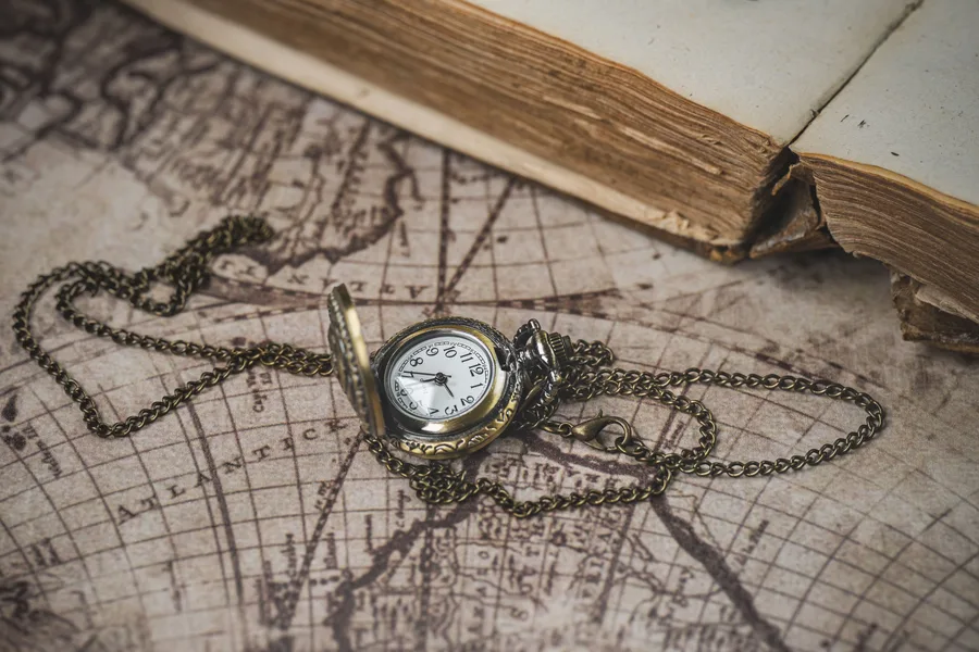 Antique pocket watch on a vintage world map beside an old book